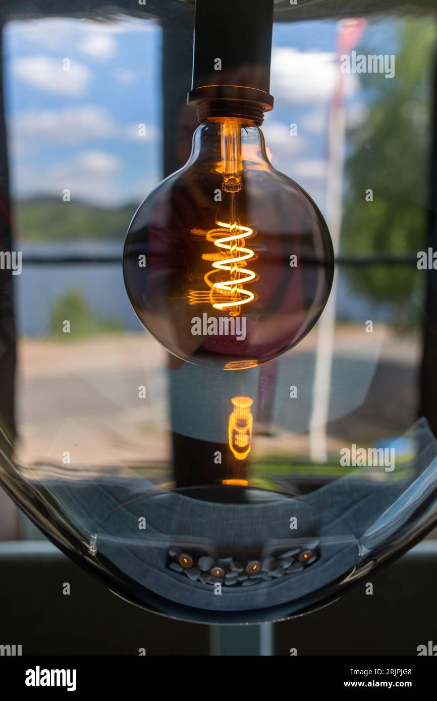 Eine Glühbirne in einer durchsichtigen Glasvase, die vor dem Hintergrund eines Fensters beleuchtet wird Stockfoto