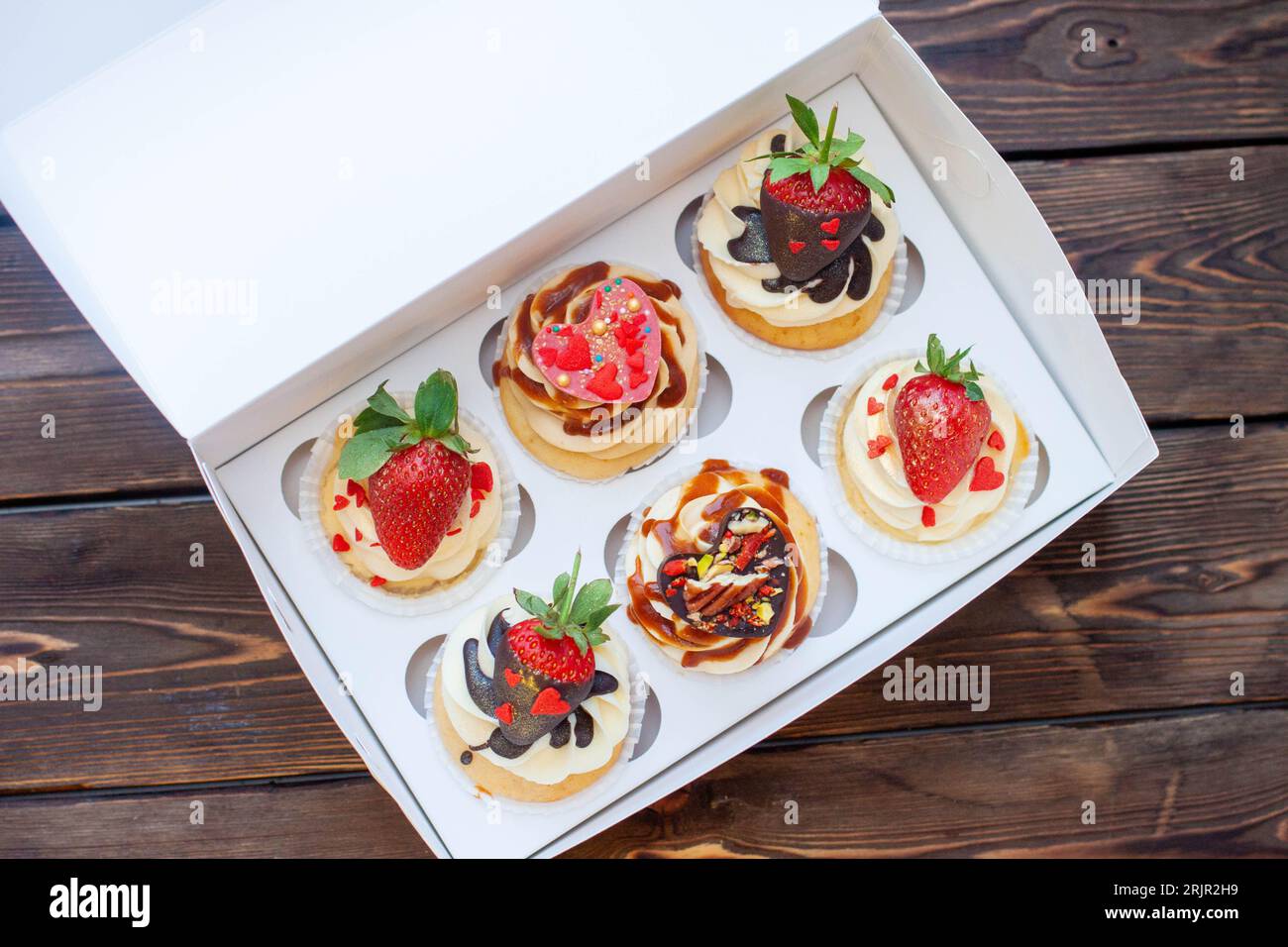 Saftige Cupcakes zum Valentinstag mit Erdbeere, eingetaucht in geschmolzene Schokolade, Schokoladenherzen, rote Streusel in Herzform Stockfoto