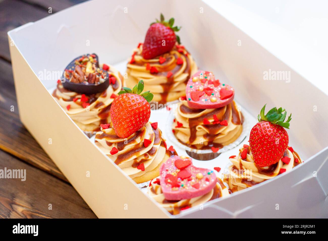 Saftige Cupcakes zum Valentinstag mit Erdbeere, eingetaucht in geschmolzene Schokolade, Schokoladenherzen, rote Streusel in Herzform Stockfoto