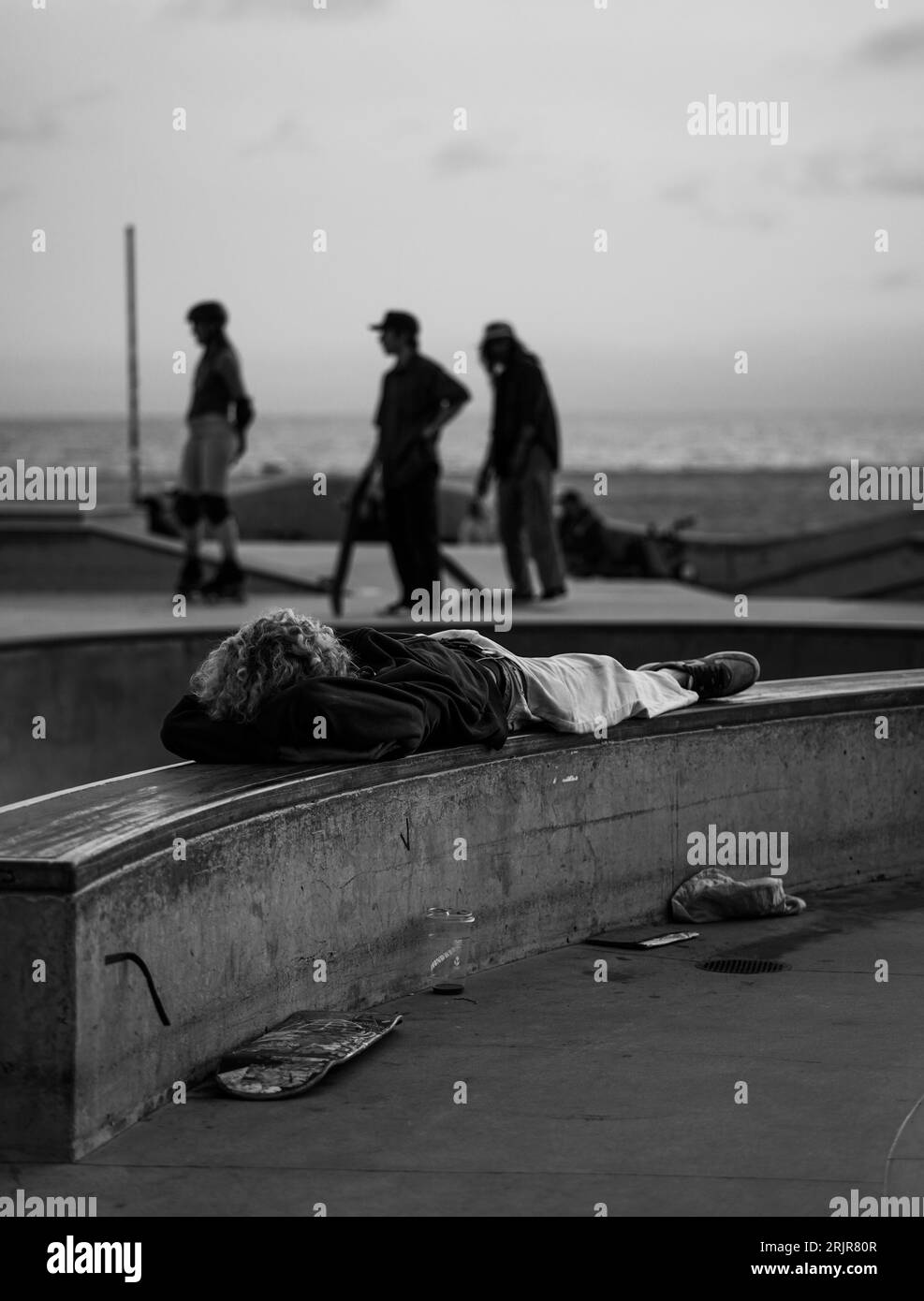 Ein junger Mann in entspannter Ruhe auf einer Skate Park Bank, in einem weißen T-Shirt und einer blauen Jeans Stockfoto