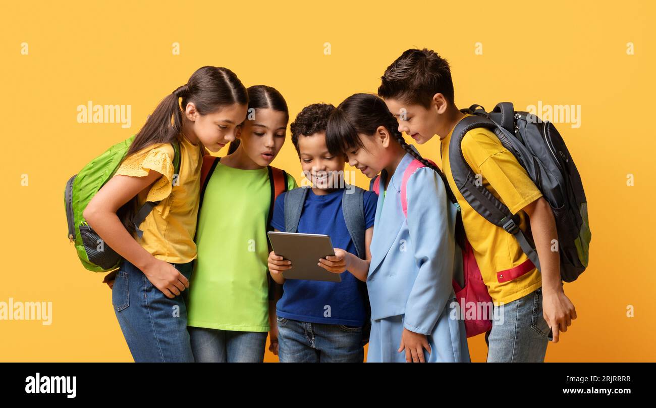 Eine Gruppe multikultureller Kinder mit Rucksäcken schaut in ein Tablet Stockfoto