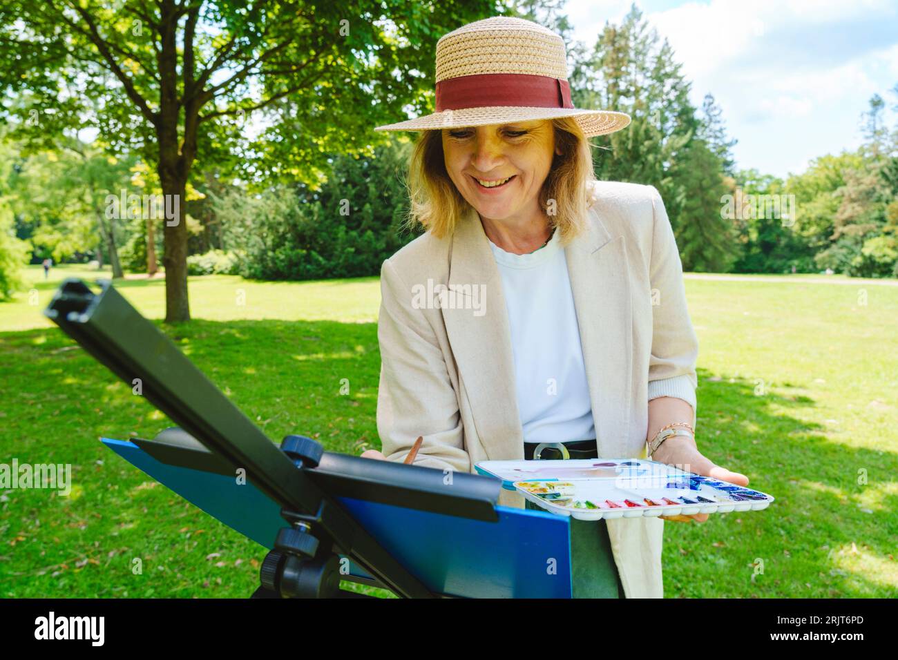 Glückliche Frau, die im öffentlichen Park einen Hut auf Leinwand trägt Stockfoto