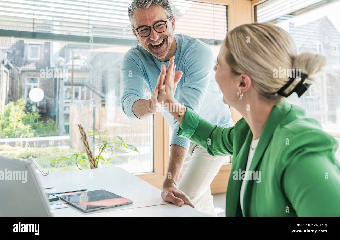 Ein fröhlicher Geschäftsmann, der einer Geschäftsfrau im Büro High-Five gibt Stockfoto