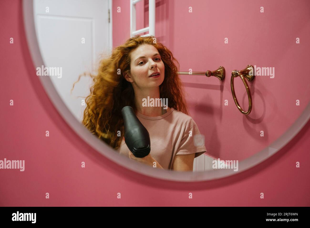 Frau, die Haare trocknet und zu Hause in den Spiegel schaut Stockfoto