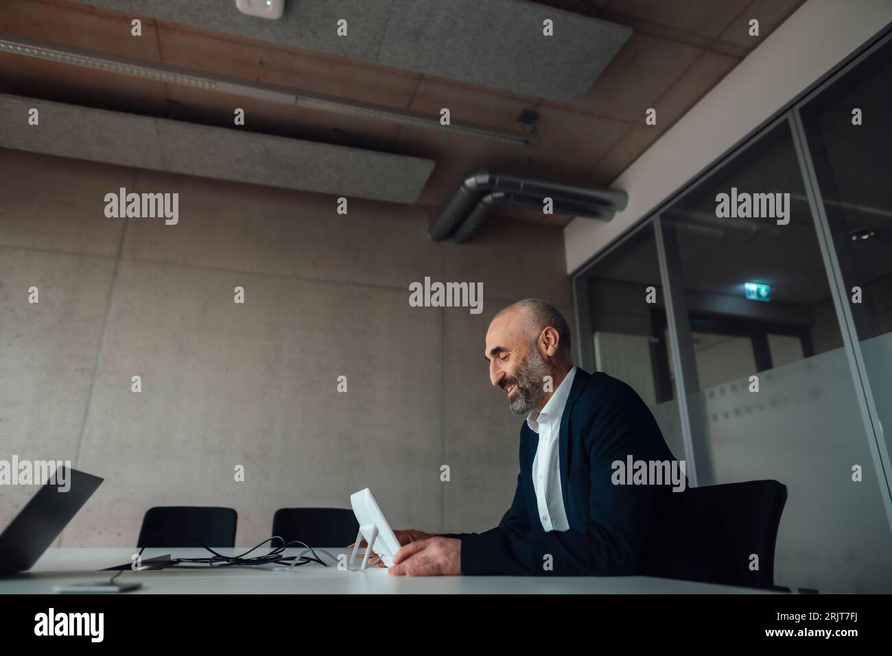 Lächelnder, reifer Geschäftsmann, der Tablet-PC am Schreibtisch nutzt Stockfoto