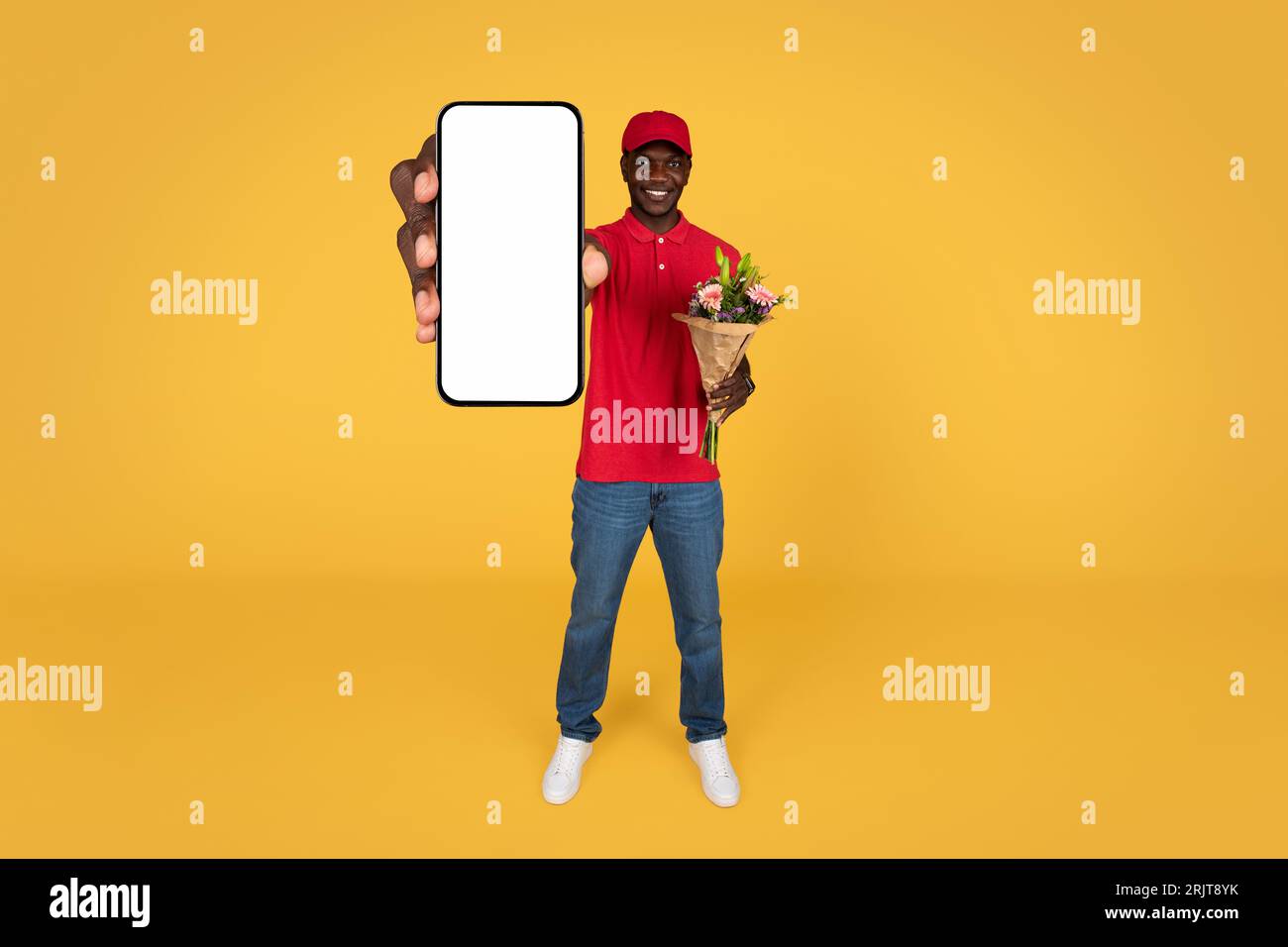 Lächelnder, tausendjähriger, afroamerikanischer Boy-Kurier in Uniform, Blumenstrauß, Telefon mit leerem Bildschirm Stockfoto