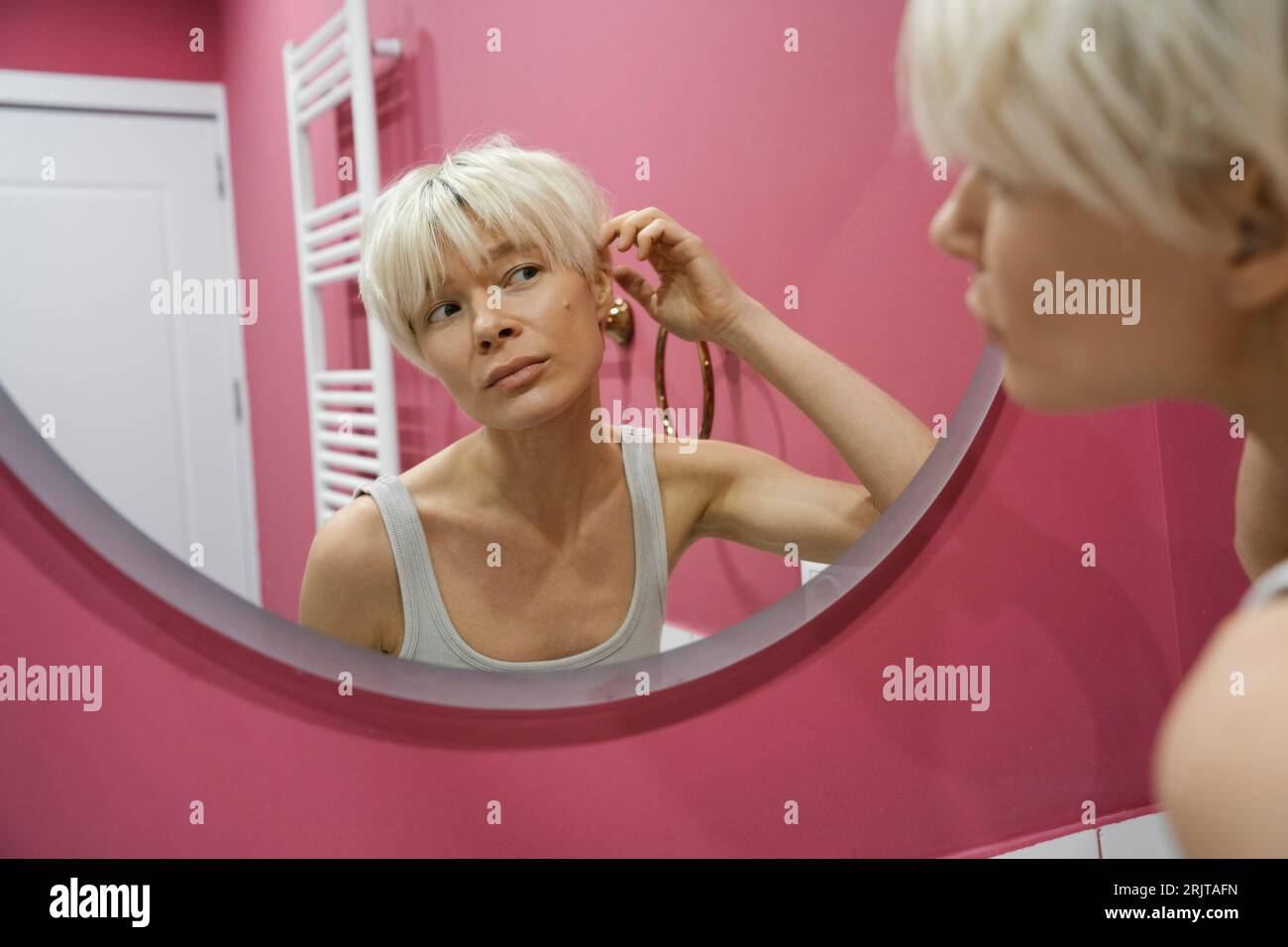 Reflexion einer blonden Frau, die Haare im Badezimmer berührt Stockfoto