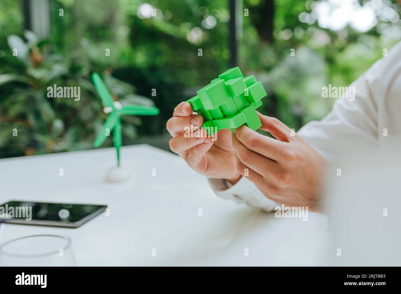 Hände eines Geschäftsmannes mit grünem Puzzlewürfel am Schreibtisch im Büro Stockfoto