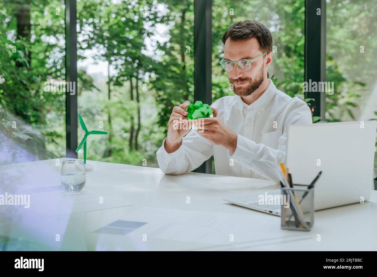 Geschäftsmann löst grünen Puzzlewürfel am Schreibtisch im Büro Stockfoto