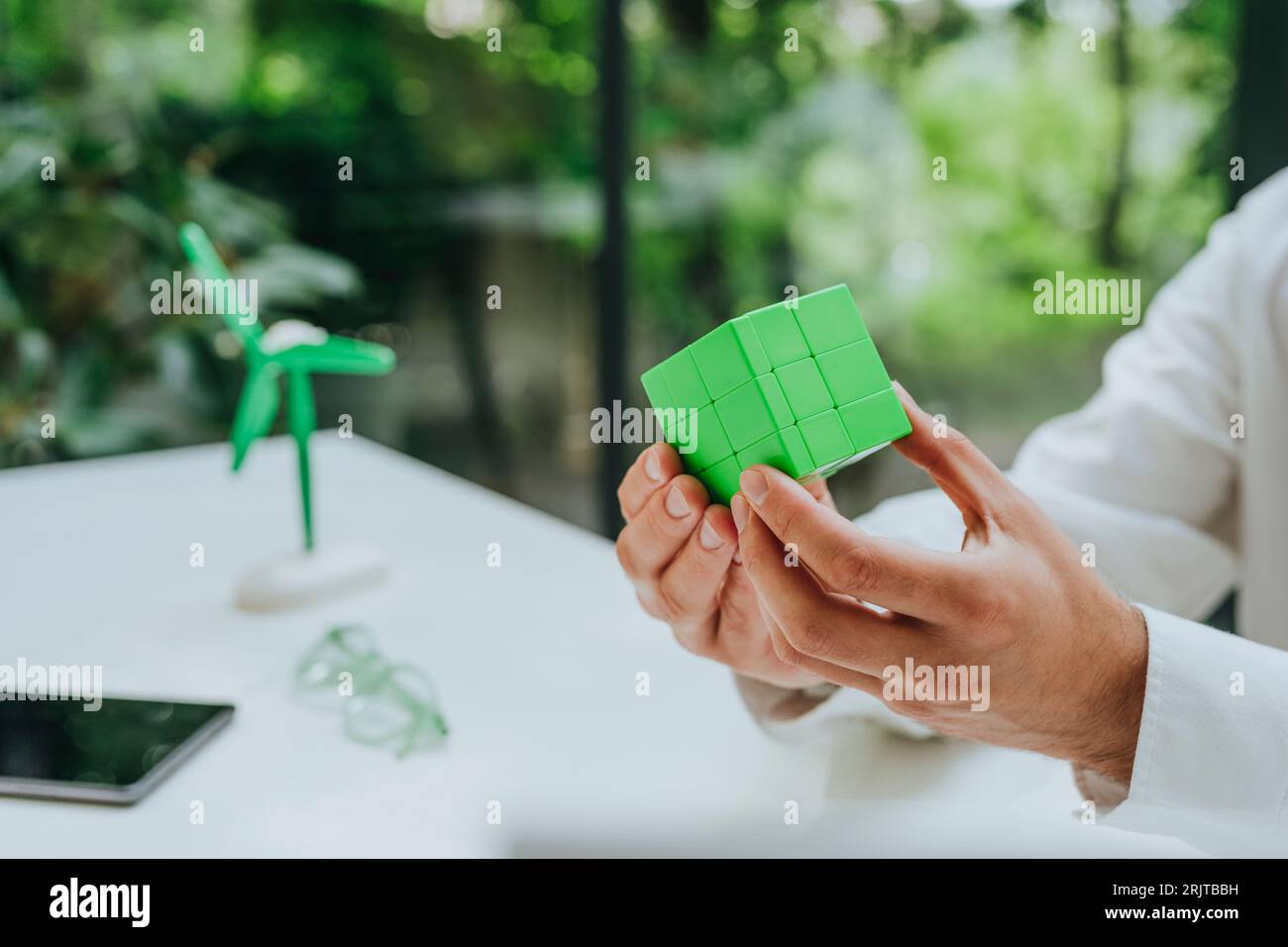 Hände eines Geschäftsmannes mit grünem Puzzlewürfel am Schreibtisch Stockfoto