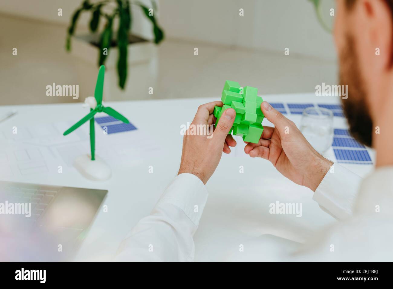 Geschäftsmann löst grünen Puzzlewürfel am Schreibtisch Stockfoto
