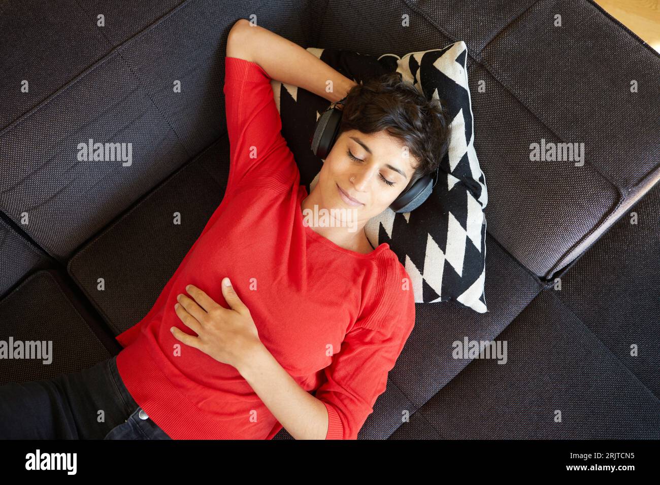 Diese Frau lässt sich stilvoll entspannen und lässt sich mit ihren Kopfhörern auf der Couch entspannen Stockfoto