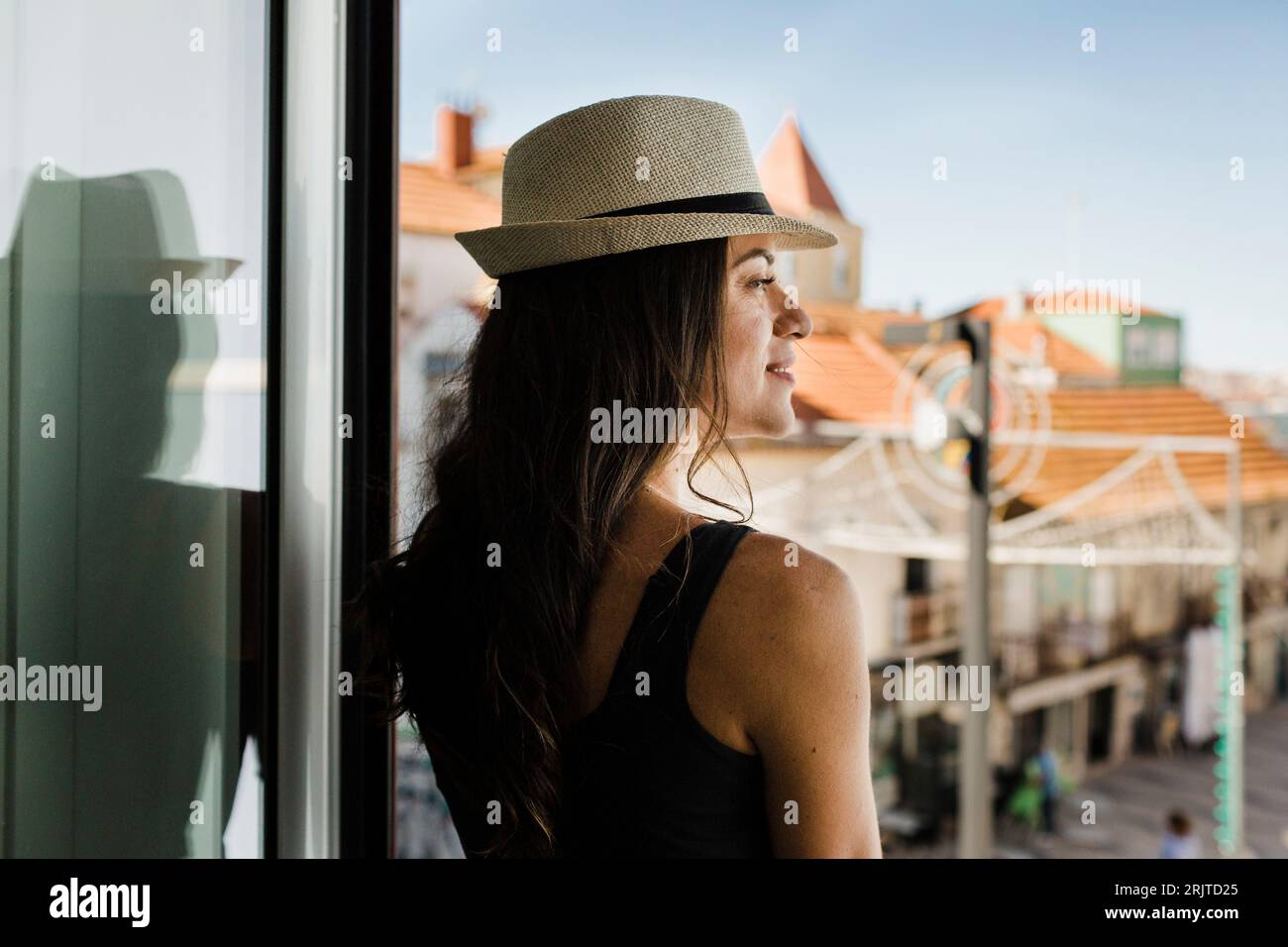 Nachdenkliche junge Frau mit Hut, die durch das Fenster schaut Stockfoto