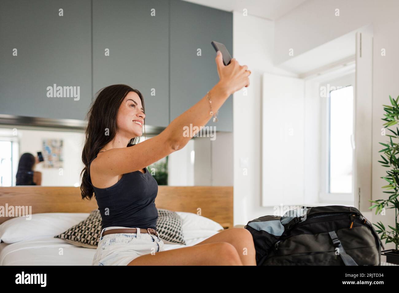 Glückliche junge Frau, die Selfie über Smartphone im Schlafzimmer nimmt Stockfoto