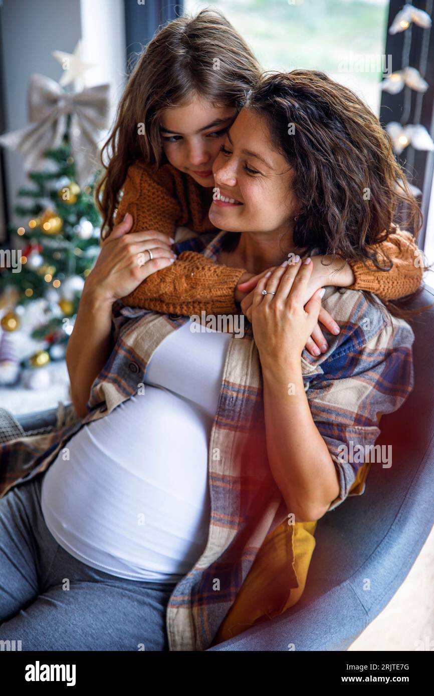 Mädchen, das die werdende Mutter umgibt, die zu Hause auf dem Stuhl sitzt Stockfoto