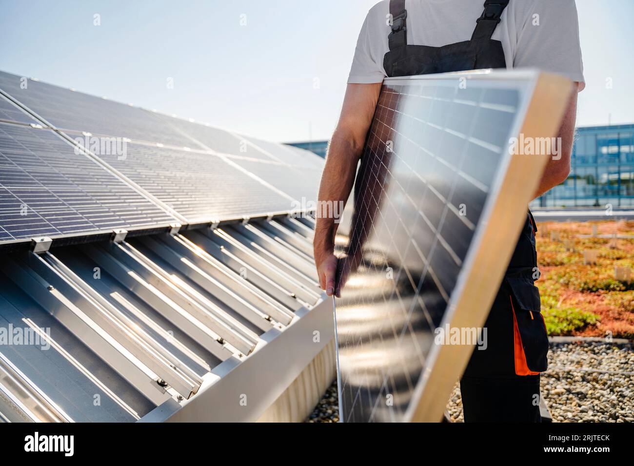 Abgeschnittene Ansicht eines Handwerkers, der Solarpanel auf dem Dach eines Firmengebäudes hält Stockfoto