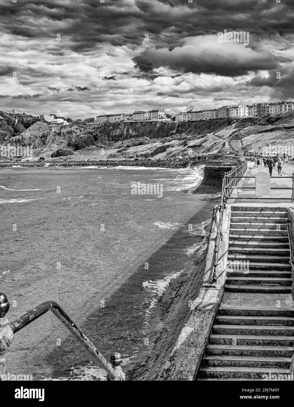 Eine Treppe führt zu einer Promenade am Meer. Der Hügel oben wird von einer Reihe von Hotels mit weißer Fassade gekrönt. Wellen prallen gegen eine Meeresmauer. Stockfoto