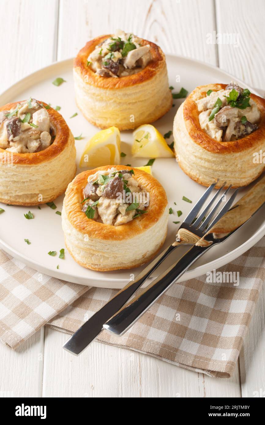 Leckeres Blätterteig vol-au-Vent gefüllt mit Huhn, Pilzen und Sahne auf dem Teller auf dem weißen Holztisch. Vertikal Stockfoto