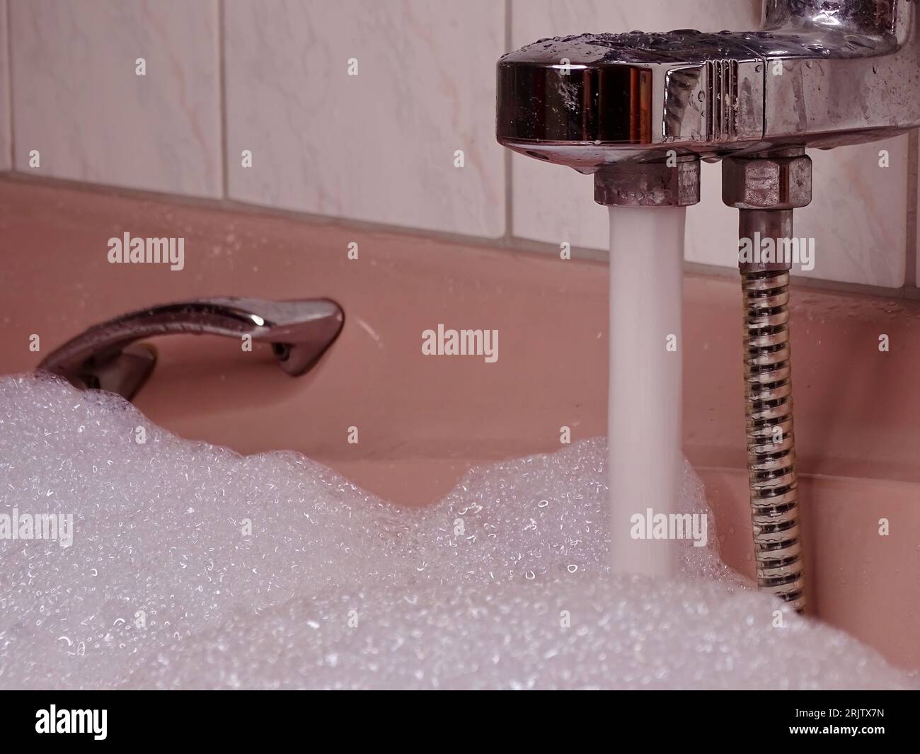 Rosafarbene Badewanne bis zum Rand gefüllt: Metallischer Wasserhahn fließt mit Wasser und reichlich Schaum Stockfoto