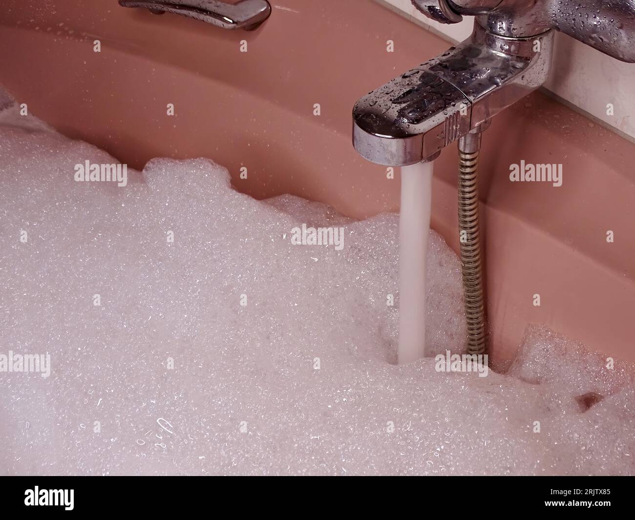 Rosafarbene Badewanne bis zum Rand gefüllt: Metallischer Wasserhahn fließt mit Wasser und reichlich Schaum Stockfoto