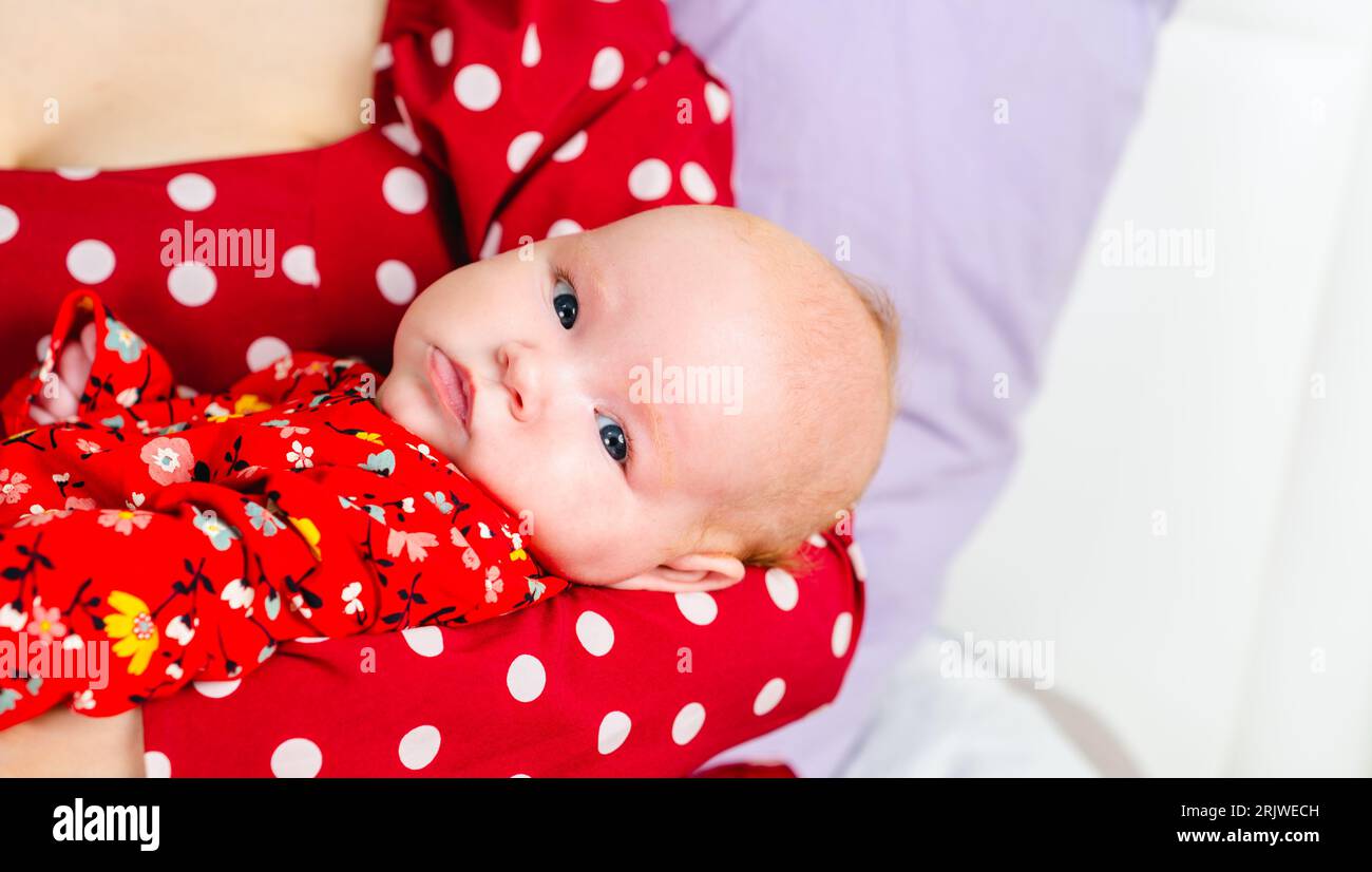 Neugeborenes Mädchen an den Händen der Mutter in rotem Polka-Dot-Kleid Stockfoto