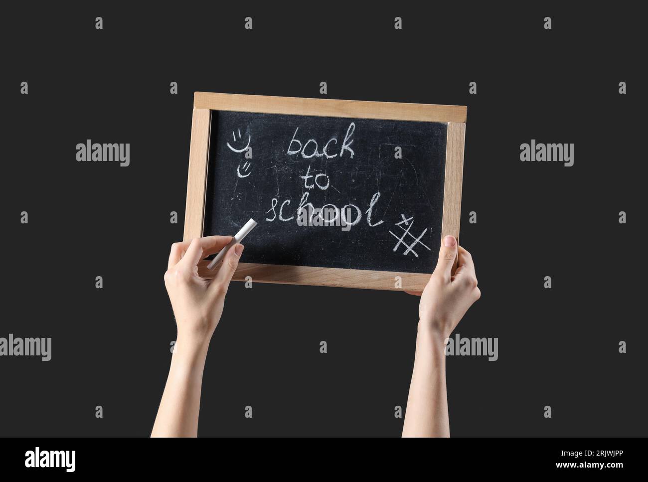 Weibliche Hände halten Kreide und Tafel mit Text ZURÜCK ZUR SCHULE auf schwarzem Hintergrund Stockfoto