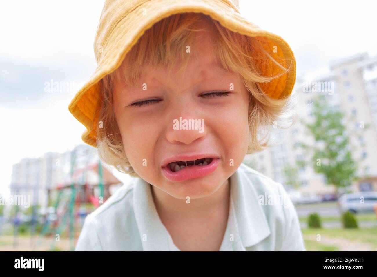 Ein kleiner trauriger Junge in einem gelben Panamahut weint auf der Straße. Stockfoto
