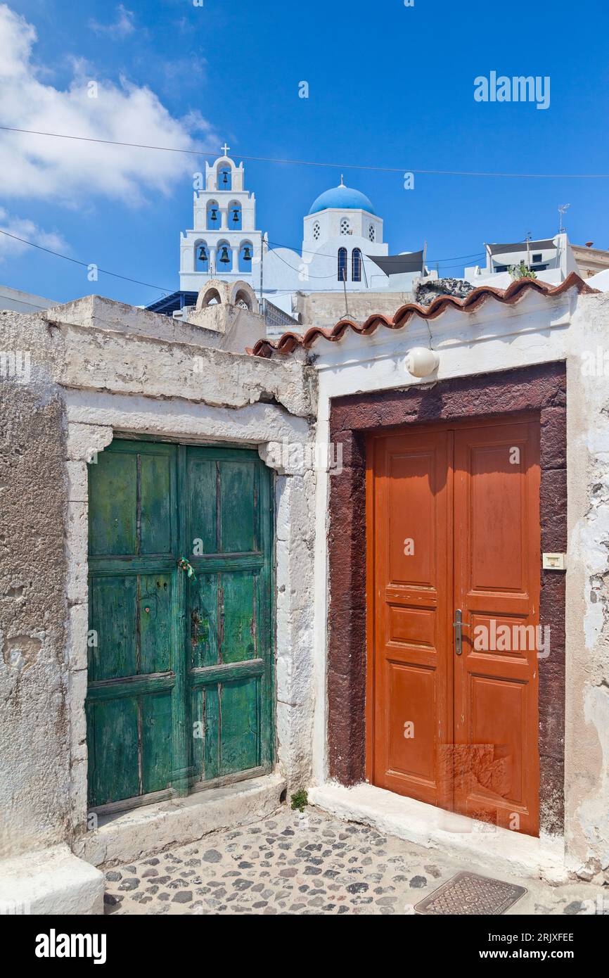 Bunte traditionelle Holztüren nebeneinander, mit der Kuppel und dem Glockenturm des Dorfes im Hintergrund, in Pyrgos Kallistis, Santorin. Stockfoto