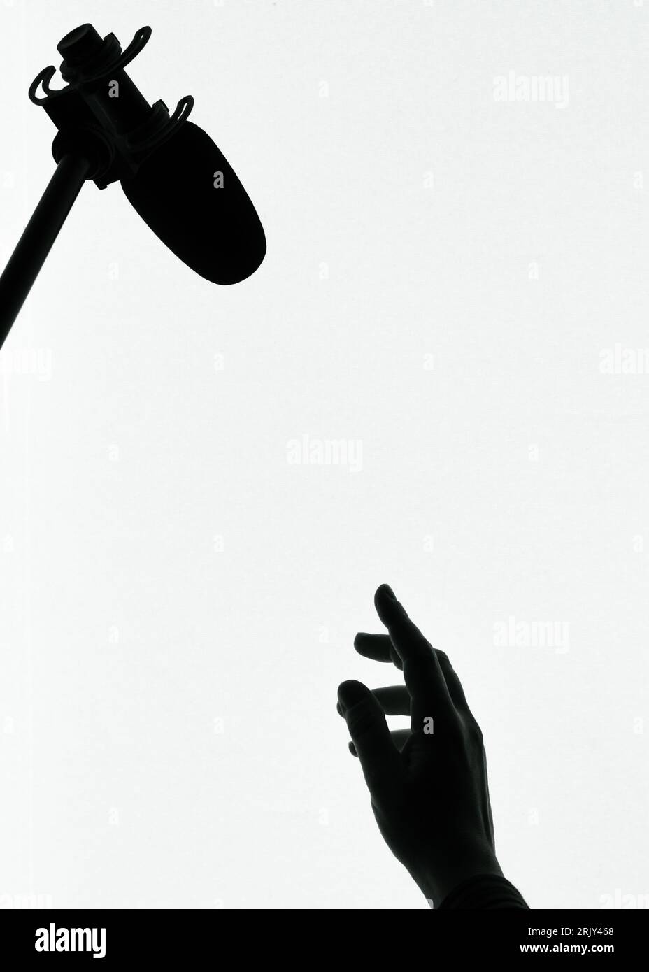 Die Silhouette der menschlichen weiblichen Hand, die bis zu einem Mikrofon reicht Stockfoto