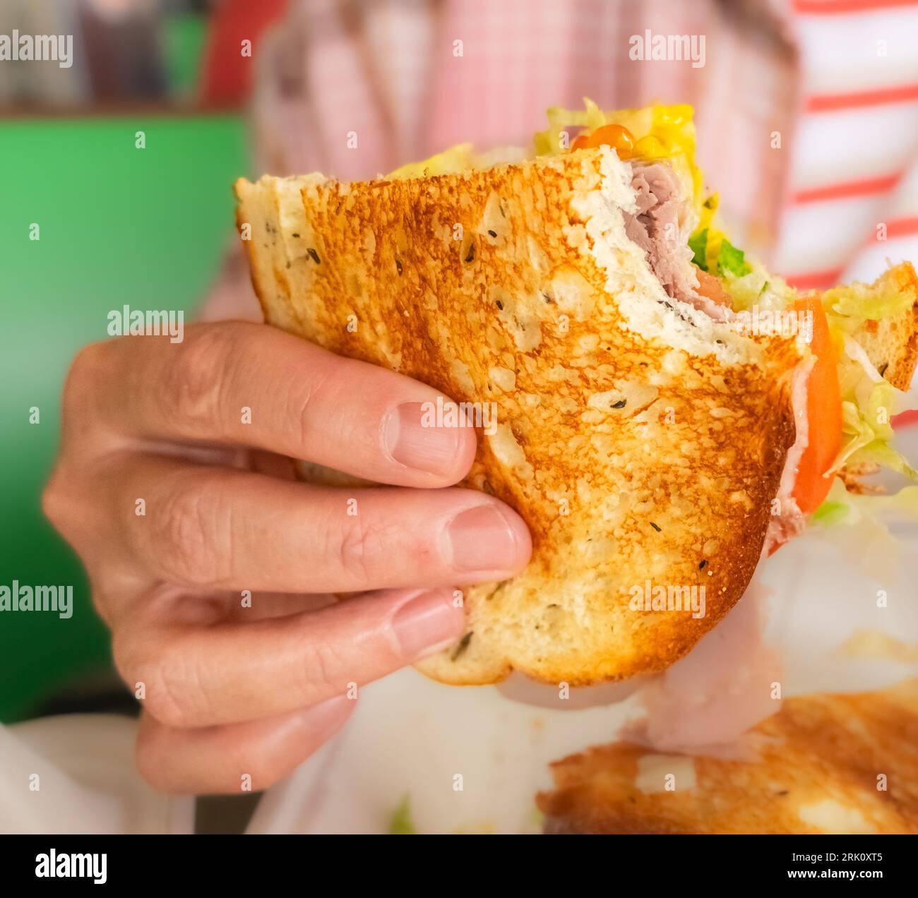 Frau mit leckerem Rindfleisch-Sandwich in der Hand. Frau, die Burger-Sandwich isst. Fastfood-Konzept. Person, die leckeres gegrilltes Sandwich mit Gemüse hält. Fe Stockfoto