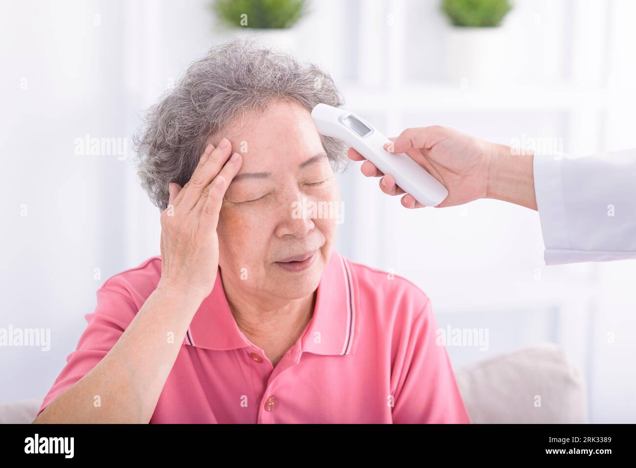 Pflegekraft misst Temperatur an Seniorin mit Digitalthermometer Stockfoto