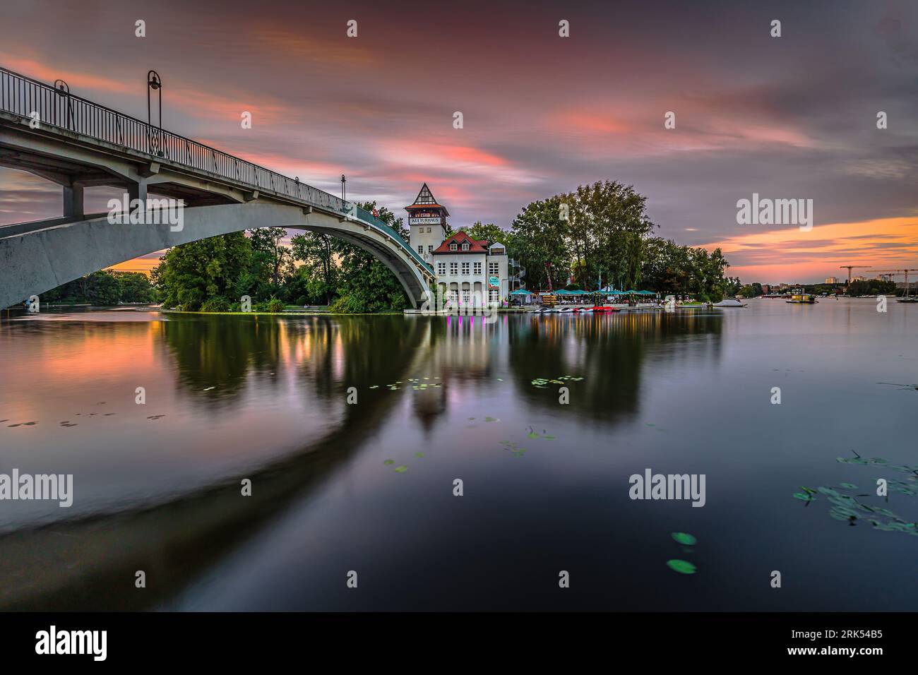 Sonnenuntergang in Berlin mit farbenfrohem Himmel. Brücke über die Spree zur Insel der Jugend am Abend im Sommer. Beleuchtetes Kulturhaus mit Biergarten Stockfoto