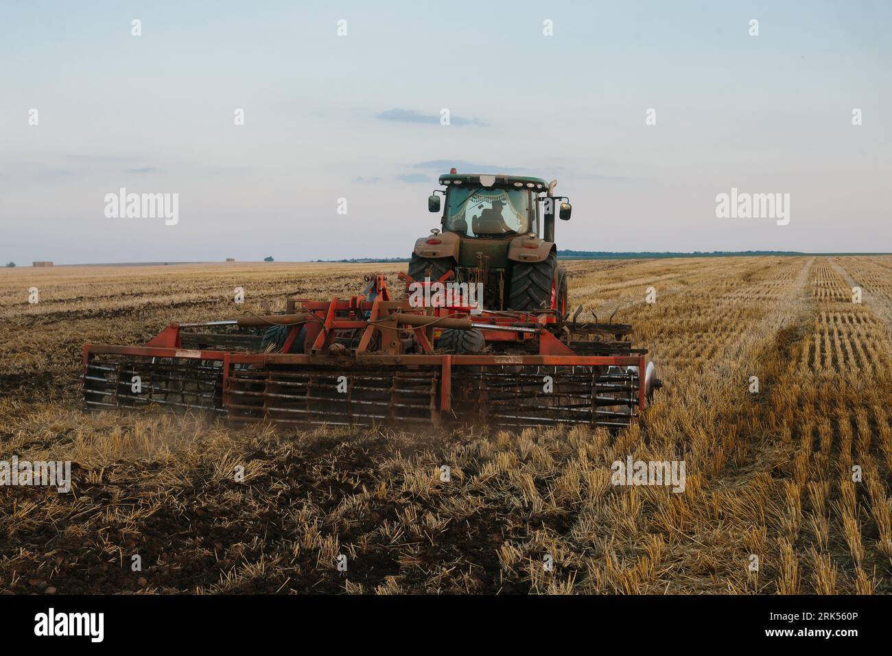Der moderne Traktor mit einer schweren gezogenen Scheibenegge befährt ein weites hügeliges Feld. Landwirtschaftskampagne im Herbst oder Frühjahr Stockfoto