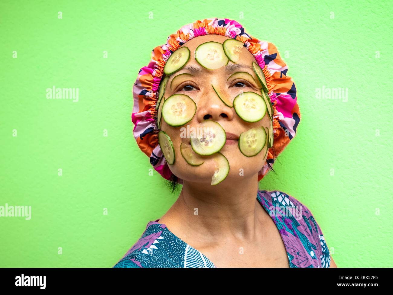 Eine Kopf-Schulter-Seite mit Blick auf eine vietnamesische asiatische Frau mit Gurken-Schönheitsbehandlung im Gesicht und mit Duschhaube. Stockfoto
