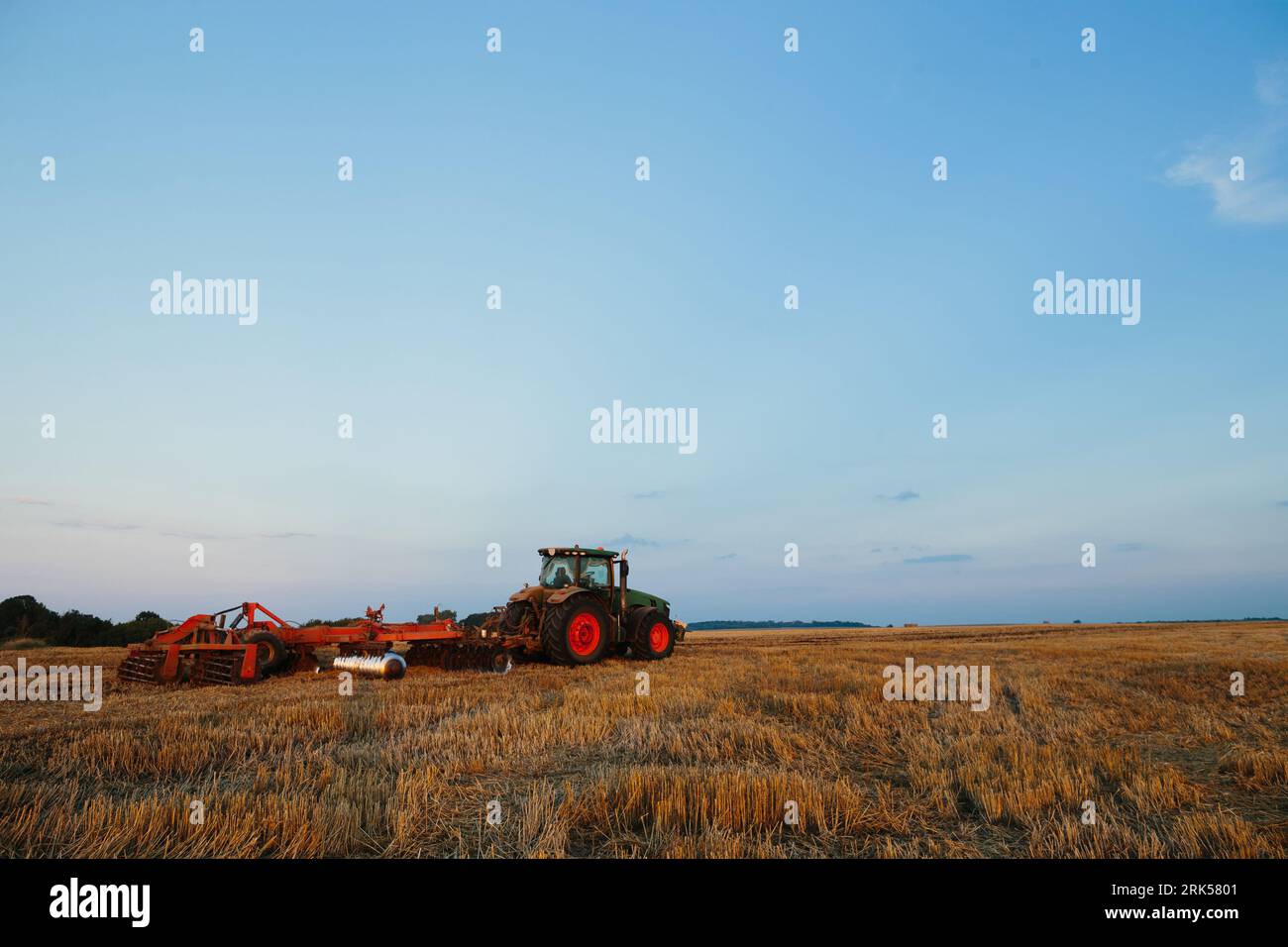 Der moderne Traktor mit einer schweren gezogenen Scheibenegge befährt ein weites hügeliges Feld. Landwirtschaftskampagne im Herbst oder Frühjahr Stockfoto