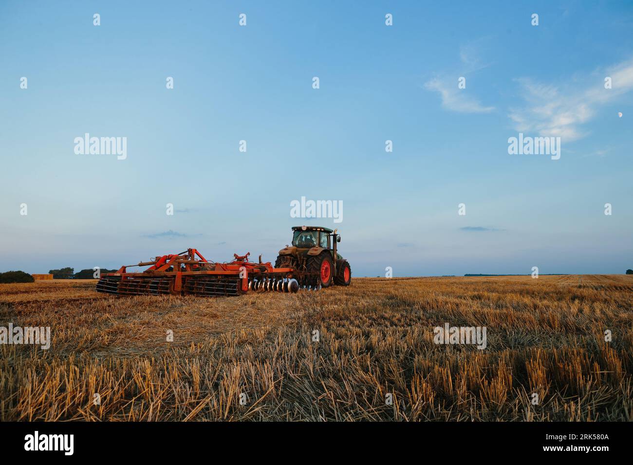 Der moderne Traktor mit einer schweren gezogenen Scheibenegge befährt ein weites hügeliges Feld. Landwirtschaftskampagne im Herbst oder Frühjahr Stockfoto