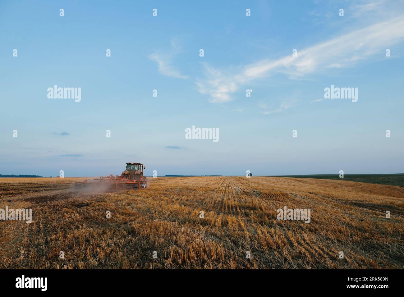 Der moderne Traktor mit einer schweren gezogenen Scheibenegge befährt ein weites hügeliges Feld. Landwirtschaftskampagne im Herbst oder Frühjahr Stockfoto