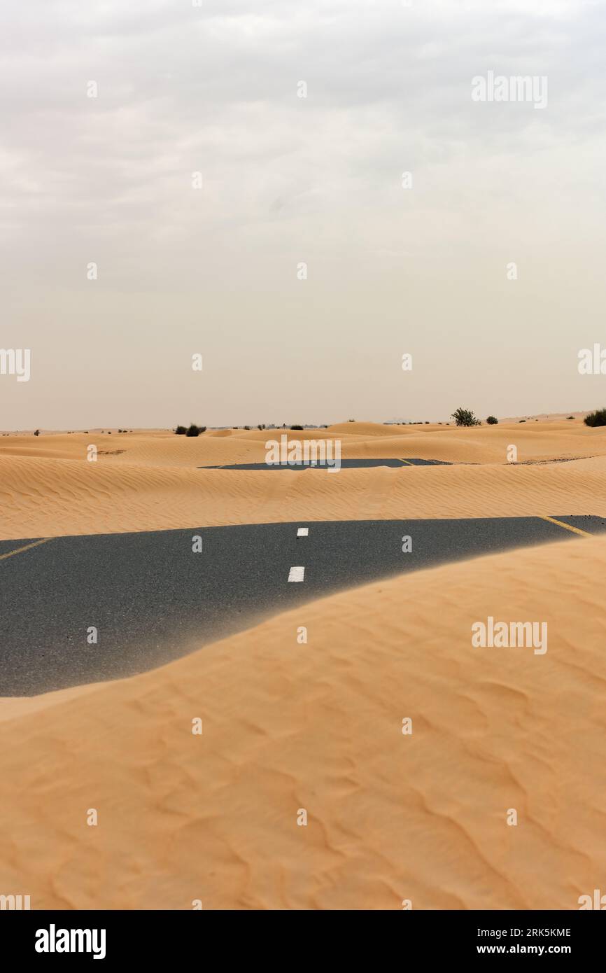 (Selective focus) Stunning view of a deserted road covered by sand dunes. Empty road that run through the Dubai desert. Dubai, United Arab Emirates. Stockfoto