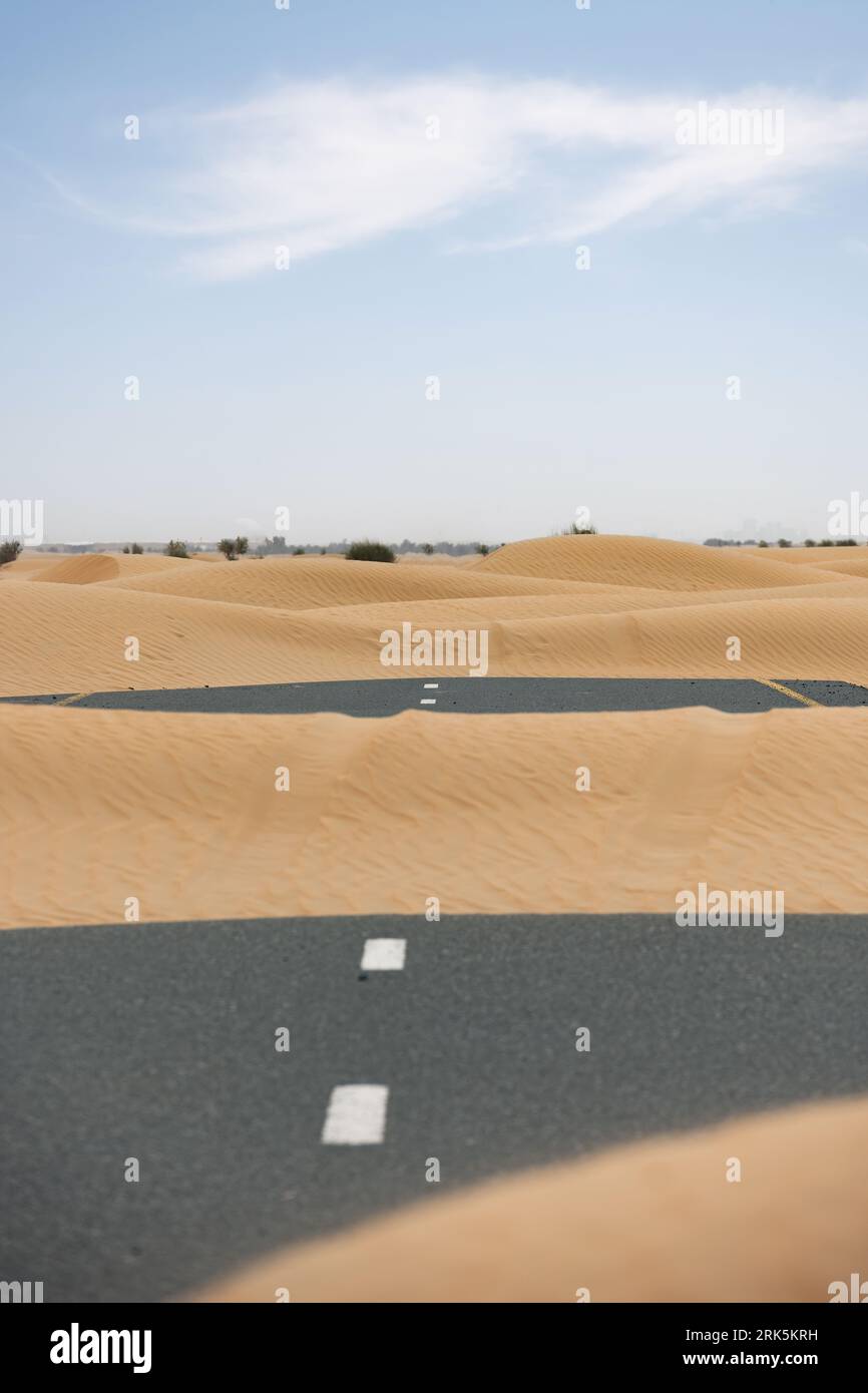 (Selective focus) Stunning view of a deserted road covered by sand dunes. Empty road that run through the Dubai desert. Dubai, United Arab Emirates. Stockfoto