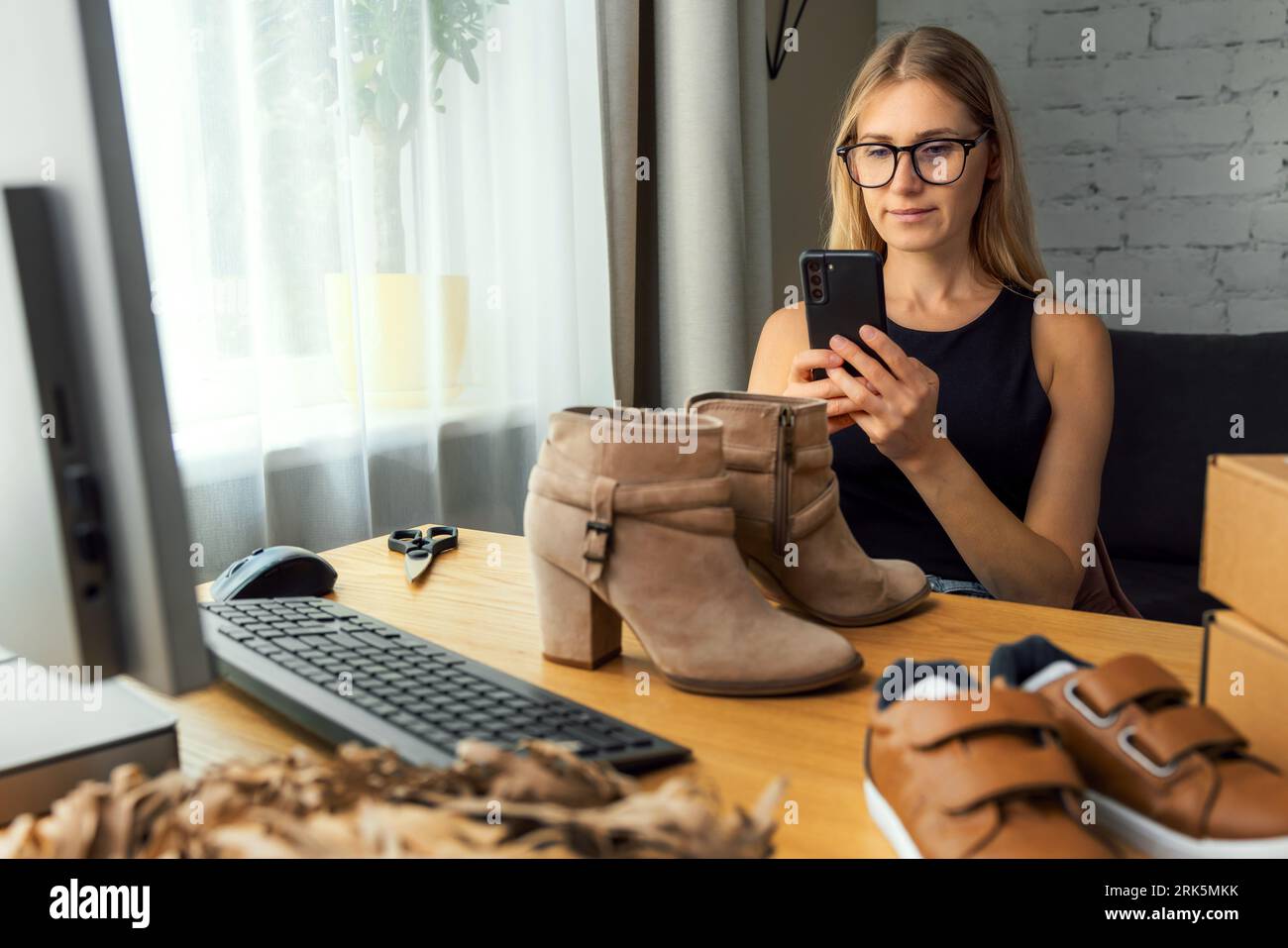 Frau, die zu Hause Fotos mit dem Handy von Schuhen für ihren Online-Shop macht. Eigentümer eines kleinen Unternehmens Stockfoto