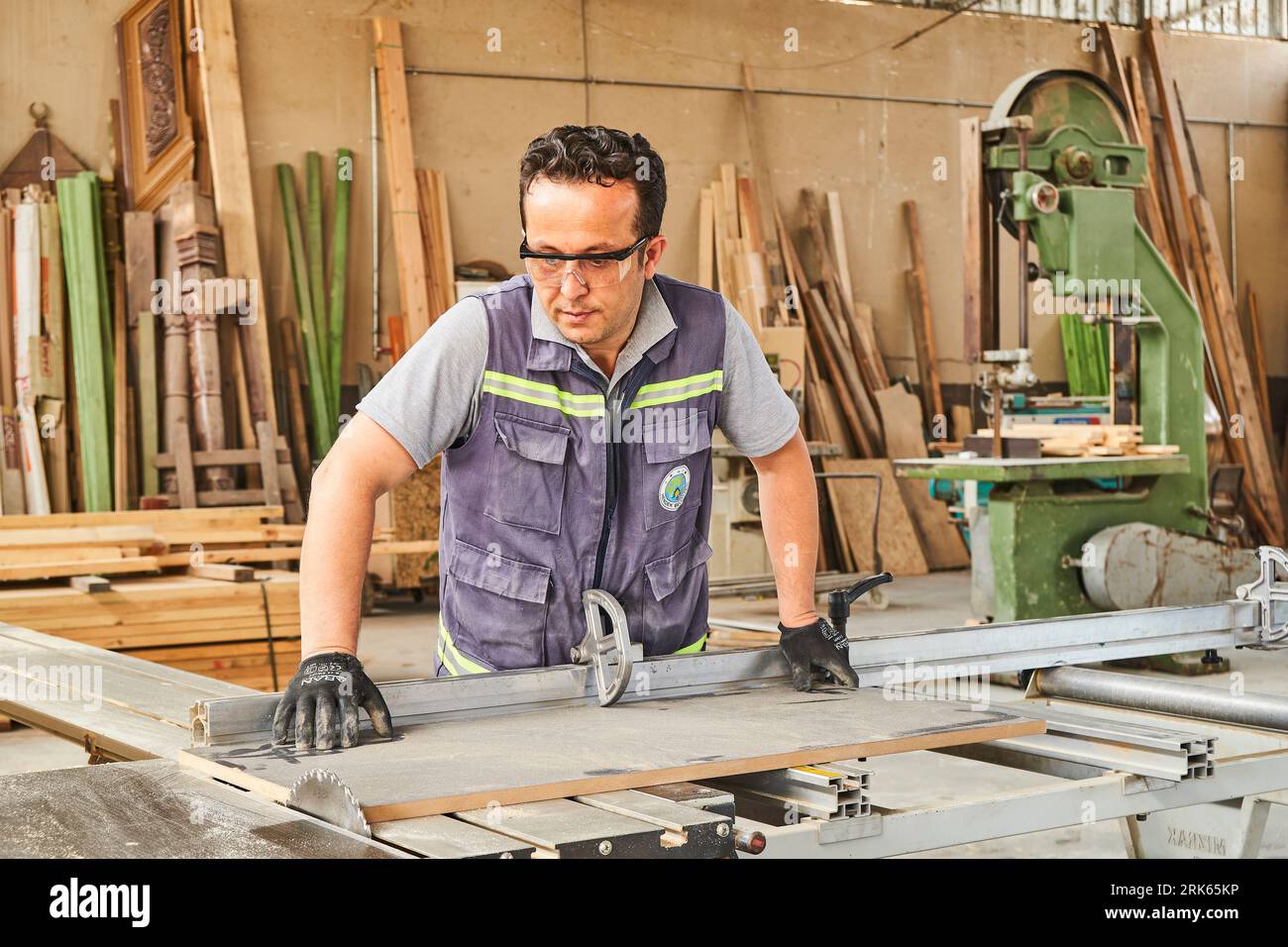 Zimmermann, der Holz in einer Werkstatt bearbeitet. Männlicher Arbeiter mit Maske und Sicherheitsweste. Zimmerei Stockfoto