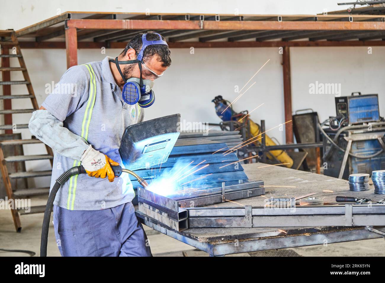 Arbeitender Mann in einer Werkstatt/Fabrik. Mann, der an Metall arbeitet. Metallbearbeitung. Eisenschweißen und Einsatz von Industrieanlagen Stockfoto
