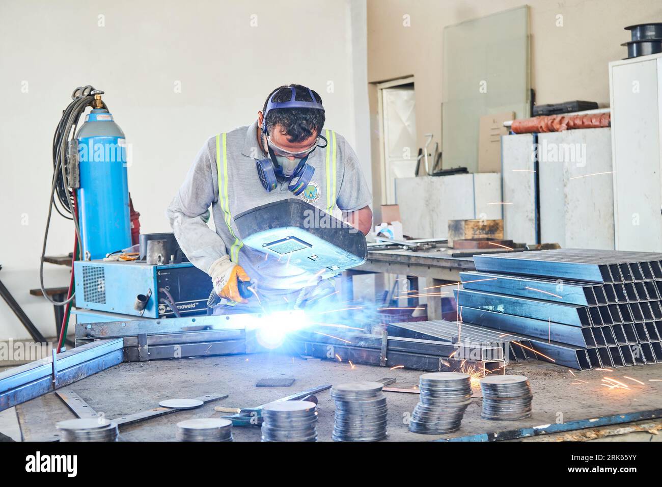 Arbeitender Mann in einer Werkstatt/Fabrik. Mann, der an Metall arbeitet. Metallbearbeitung. Eisenschweißen und Einsatz von Industrieanlagen Stockfoto