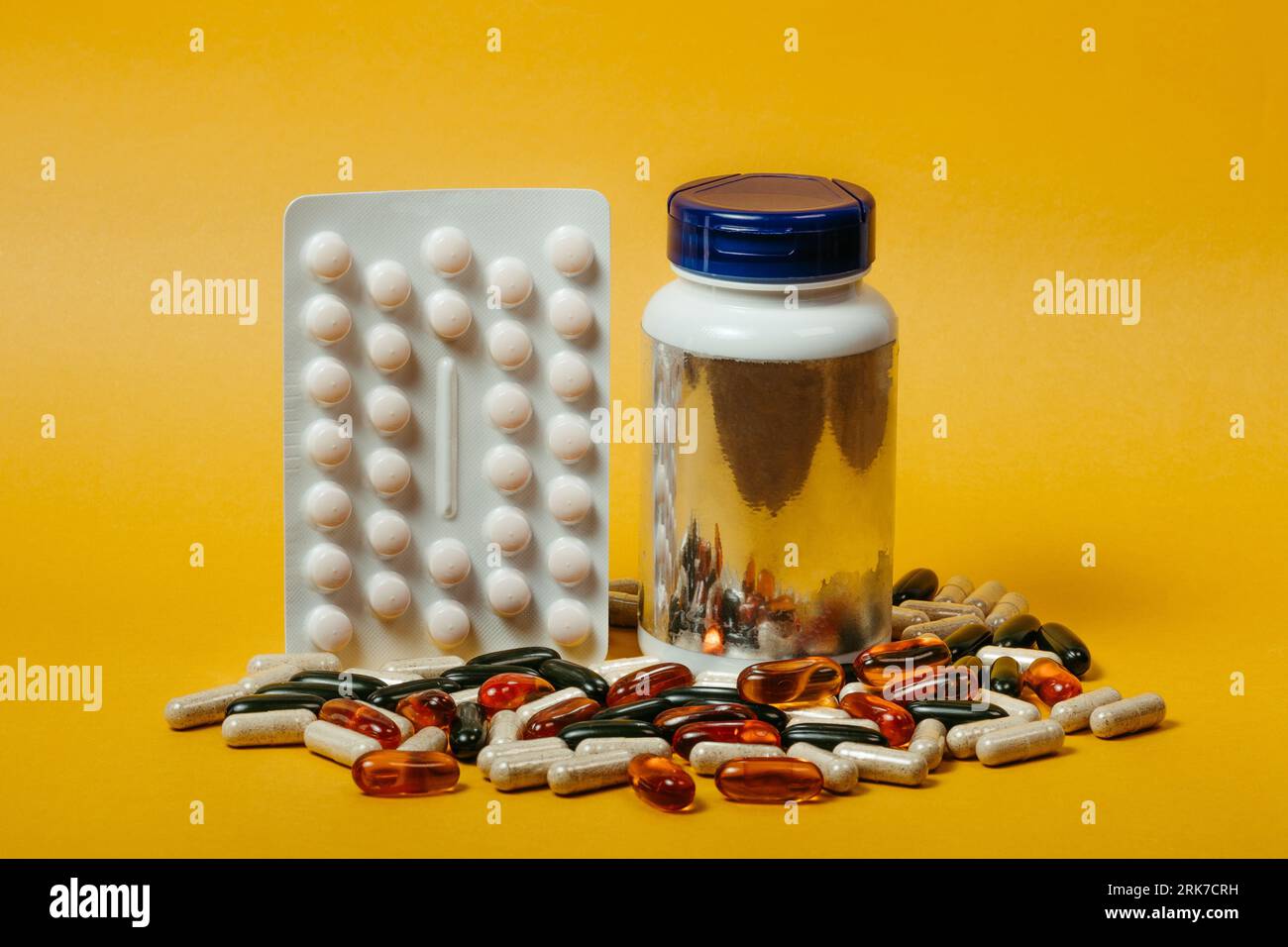 Ein Glas, das mit Vitaminergänzungskapseln auf gelbem Hintergrund gefüllt ist Stockfoto