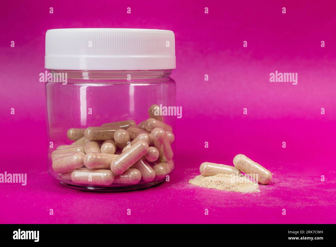 Ein Glas, das mit Vitaminergänzungskapseln auf rosafarbenem Hintergrund gefüllt ist Stockfoto