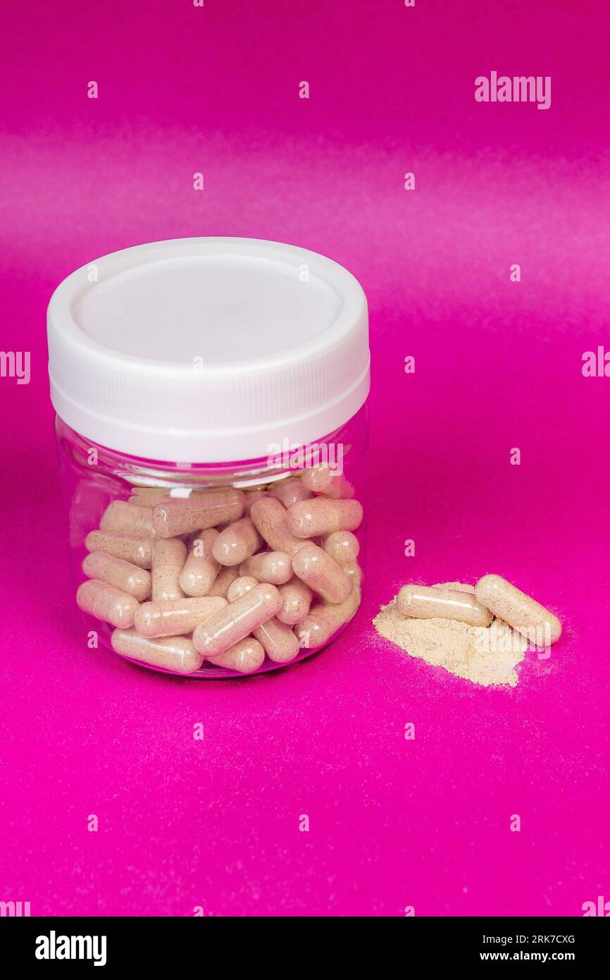 Ein Glas, das mit Vitaminergänzungskapseln auf rosafarbenem Hintergrund gefüllt ist Stockfoto