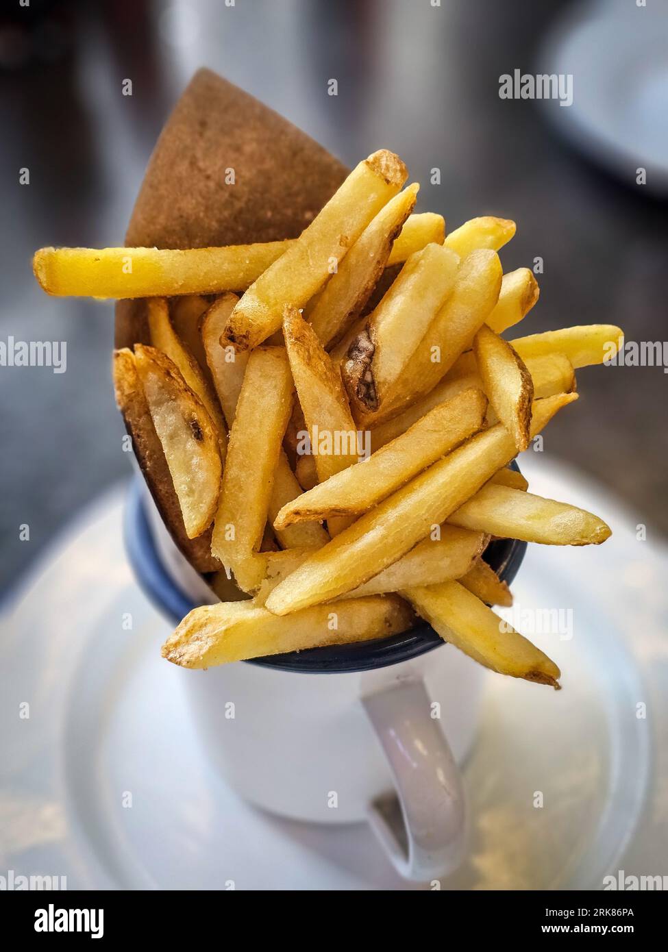 Eine kleine Schüssel und Untertasse mit einem Haufen goldener Pommes frites aus der Nähe. Stockfoto