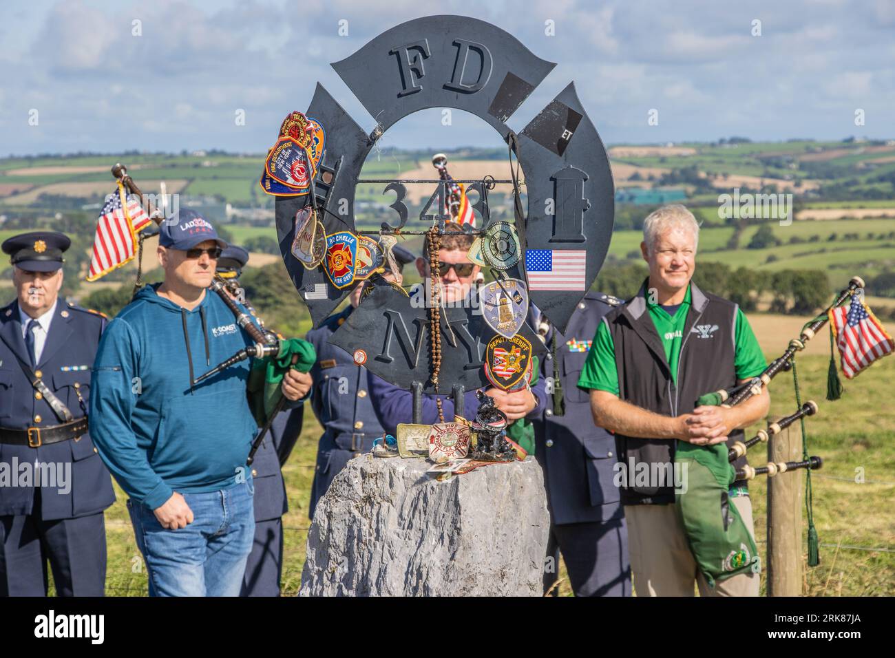 New York Firefighters und die Emerald Pipe und Drums besuchen den Gedenkgarten für gefallene Feuerwehrleute von 9/11 in Ringfinnan, Kinsale Co Cork, Irland. Stockfoto