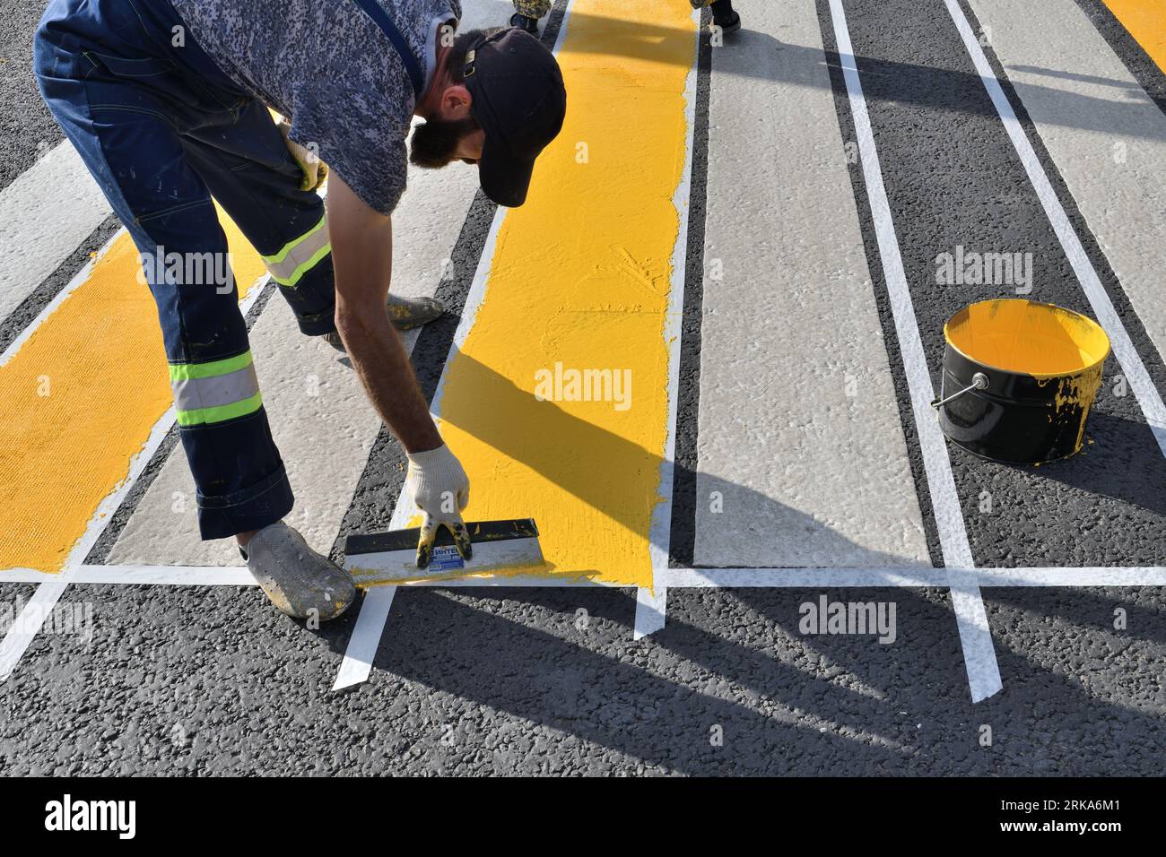 Moskau, Russland – 21. August. 2023. Der Arbeiter trägt an einer Fußgängerüberquerung in Zelenograd gelbe Farbe mit Spachtel auf den Asphalt auf Stockfoto