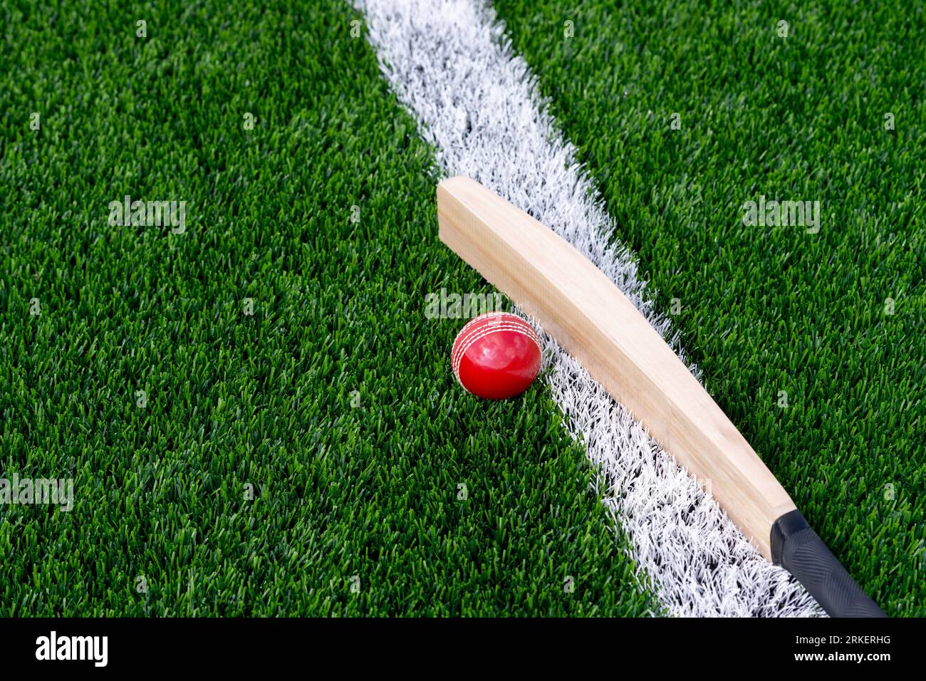 Cricketschläger und roter Ball mit natürlichem Licht auf grünem Gras. Horizontales Sportposter, Grußkarten, Kopfzeilen, Website und App Stockfoto